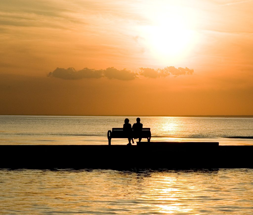 Couple seated on a bench overlooking the ocean at sunrise. They are taking time to be close when marriage feels distant